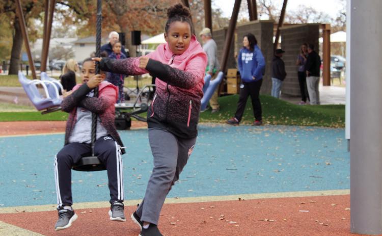 Twins Alexia and Nadine Nsabimana, age 8, of Shawnee, have fun on the rope swing merry-go-round during the Woodland Veterans Park Grand Re-Opening on Nov. 11. Countywide & Sun/Natasha Dunagan