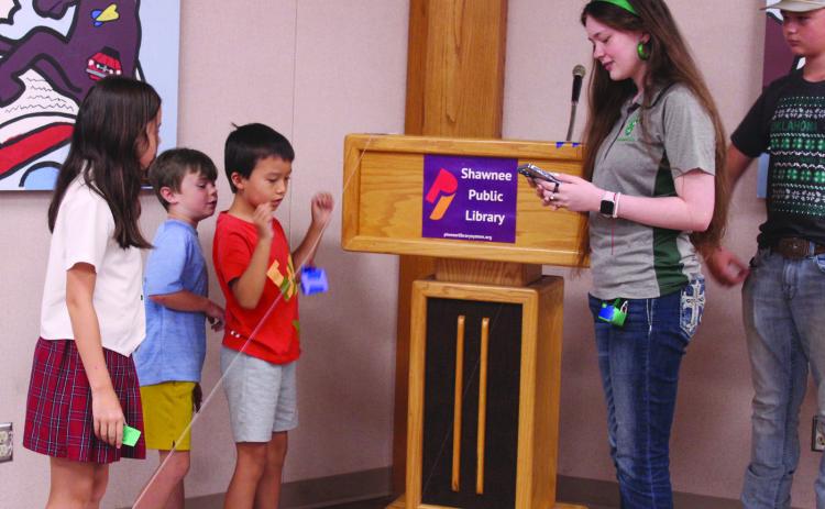 State 4-H STEM Innovator Tori Nelms watches the stopwatch on her phone as Nina Tomlin, 9; Barrett Gates, 8; and Norimi Tomlin, 7; all of Shawnee, test their zip line container, which holds a ping pong ball, during the 'Build It: Zip Line Zoom' program at the Shawnee Public Library on July 21. Children worked together to build their containers, then tested them on six already-made zip lines made of cotton string or fishing line. Fellow Innovators Madison Maddox & Tony Nelms, plus 4-H Educator Kacie Jasper.