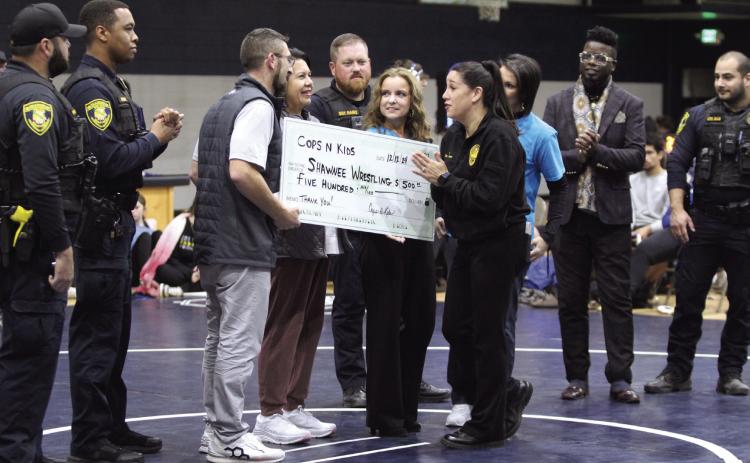 Vivian Lozano, the founder of Cops n' Kids, presents a check from the Cops n' Kids Board for $500 to Shawnee Wrestling Coach Andrew McCune for the Shawnee Wrestling Program during the home dual on Dec. 12. Lozano said the board plans to donate to different causes in the community every year. Present for the presentation, not in order, were board members Tara Andrews, Sally Coleman, Lisa Watson and Jeff Chamblain, as well as Jamelle Payne, Sgt. Rains, Cpl. Ruiz, Cpl. Price and PTL Arispe.