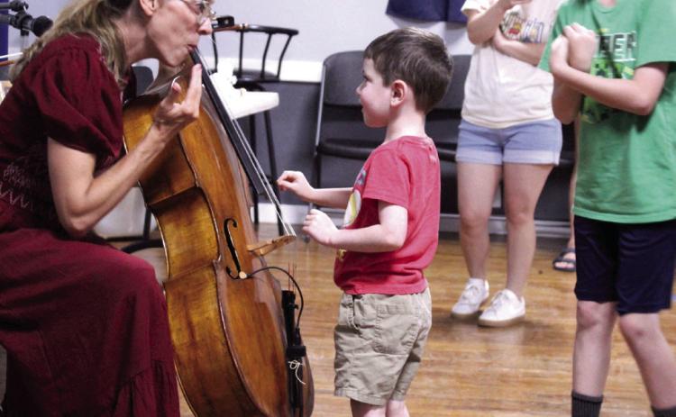 Zane Dowell, 4, of McLoud, plucks the strings on Erin Yeaman's cello and gets a reaction during the 'Tunes and Tales with Erin Yeaman' McLoud Public Library program, held on June 18 at the Ray Large American Legion Post 244. Yeaman also played her cello along to three children's books and read 'The Three Little Pigs,' as volunteers made sound effects. In addition to being a composer and voice actor, Yeaman provides music for Scholastic audio books.