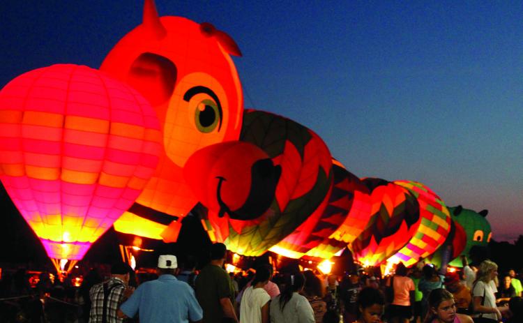 A line of hot air balloons light up on Aug. 9, 2025 - including "Milky Way," which is shaped like a cow, and a new llama-shaped balloon - during the FireLake Fireflight Balloon Festival at the CPN Festival Grounds. File photo