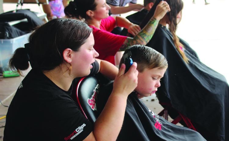 Sport Clips hair stylist Nicole Lawless talks with Keanu Christensen, 4, of Shawnee, before shaving his sideburns during the Second Annual Hug-a-thon, held at Woodland Veterans Park in Shawnee on Aug. 2. Also giving free haircuts were stylists Brittany Burden and Libertee Desordi. Natasha Dunagan, Countywide & Sun