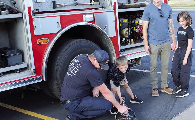 Shawnee Fire Department Sgt. Dillon McCabe lets Murphy Sayre, 6, of Shawnee, push a button to open the jaws of life, as father Garrett Sayre and sister Melody Sayre, 9, watch at the first Shawnee Safety Night: Project Safe Stop, held outside the Marty Lewis Public Safety Center at Gordon Cooper Technology Center on Sept. 3. The event was a joint effort by the Autism Foundation of Oklahoma and Shawnee Police Department to help families affected by autism. See full caption below.
