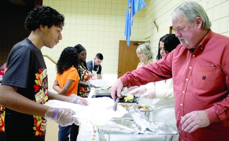 Randy Gilbert adds turkey to the dinners held by volunteer Vergil Brawner, 14, at the 19th Annual Tecumseh Family Thanksgiving Dinner, held at Tecumseh City Hall Auditorium on Nov. 28. Brawner's sister, Lyric Brawner, 10, and mother, Maud Police Chief Doneisha Brawner, shown in background, also volunteered. Also shown are Mason Blumenthal, Melissa Hewett and Annie Jo Gilbert. See full cutline below.