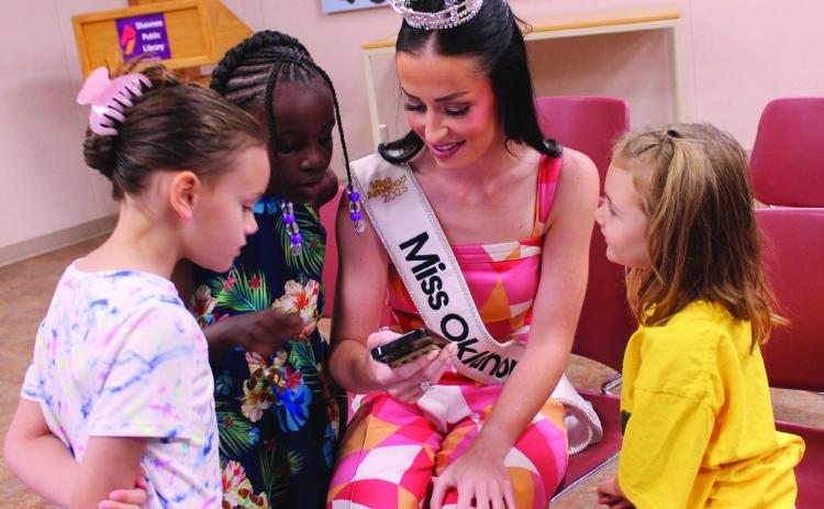 Miss Oklahoma Tessa Dorrell shows a picture of her blue pageant dress to three six-year-olds - Sarah Sprague of Tecumseh, Kenya Lightsey of Shawnee and Sibyl Hays of McLoud - during story time on July 29. Natasha Dunagan, Countywide & Sun