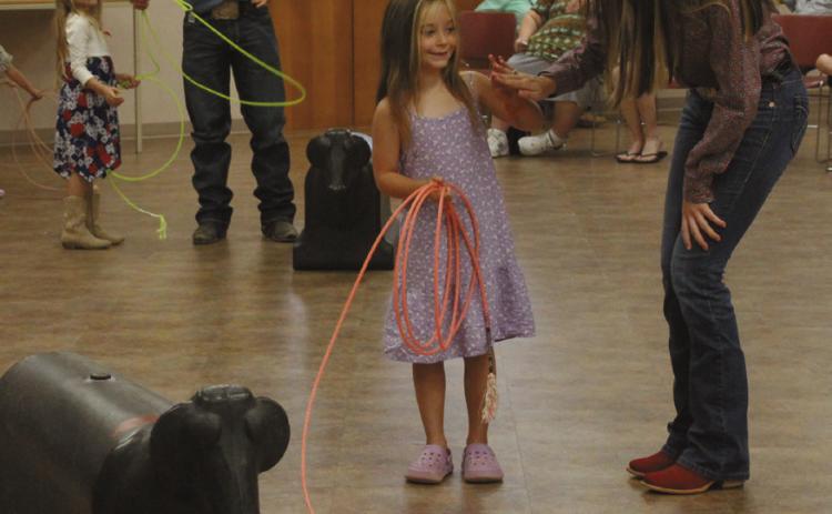 Paula Wiley, 5, of McLoud, gets a high-five from Jasey Graves after learning how to throw a lasso. Also shown is Tatum Roberts, who is helping Isabel Nunes, 6, of Shawnee. Shawnee Public Library Branch Manager Mary Sims said this is the 15th year for six IFYR youth directors to visit the library. Sims also interviewed them about their rodeo experiences, and a 'chuckwagon snack' was provided by Lindsey Cowan, Jennifer Gates and Chloe Gates of the Junior Service League.