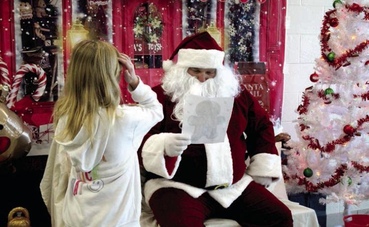 Santa looks at a coloring page completed by Lilly Hampton, 8, of Shawnee, during the Second Annual Breakfast with Santa, held at Shawnee Middle School on Nov. 30. The event was a fund-raiser for the Shawnee Wrestling Program and also included breakfast served by the wrestlers, reindeer ring toss, backgrounds for selfies and coloring stations. Countywide & Sun/Natasha Dunagan