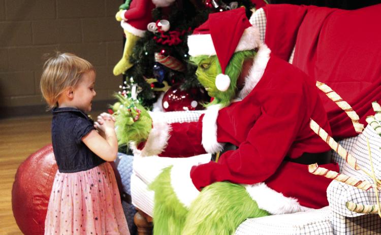 Braivlee Whitmire, 4, of Tecumseh, gives the Grinch a bracelet she made in “Whoville” before getting her picture taken with him on Dec. 8. Tecumseh Public Library employees took and printed around 200 pictures that evening at the Tecumseh City Hall Auditorium, and can be claimed at the library. Countywide &amp; Sun/Natasha Dunagan