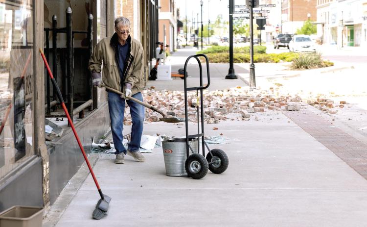 A Shawnee citizen sweeps and clears debris from in front of the Pott County Book Store in downtown Shawnee following the tornado Wednesday night. The front glass of the store as well as the west wall on the second floor was busted out or ripped from the building. Photo provided