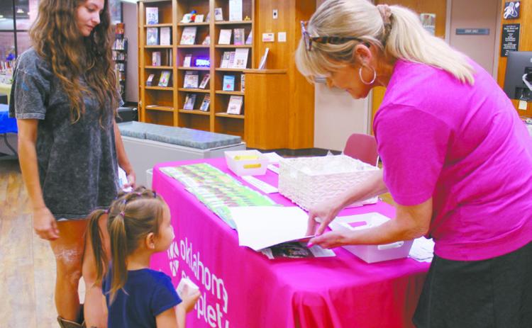 Natasha Dunagan, Countywide &amp; Sun Kathy Gooding, Community Relations Coordinator for Oklahoma Complete Health, shows a coloring book to Alice McCathern, 4, of Little Axe, as Tenisha McCathern watches during the event at Shawnee Public Library on Aug. 9. There were about 10 booths with organizations handing out school supplies and free items, in addition to an OBI blood drive.