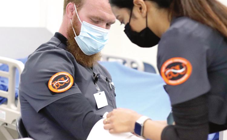 ECU Nursing student Gabriel Rebischke sits patiently while fellow student Suja Shresta practices applying bandages to his arm.