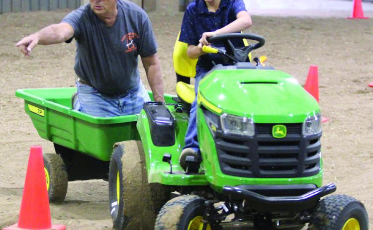 Dace Dockrey, age 9, drives a garden tractor through the obstacle course of the Peewee and Midget Tractor Operator Contest, as Fair Board Member Lynn Marlow, points to where he needs to go, on Sept. 6 at the Pottawatomie County Free Fair. File photo